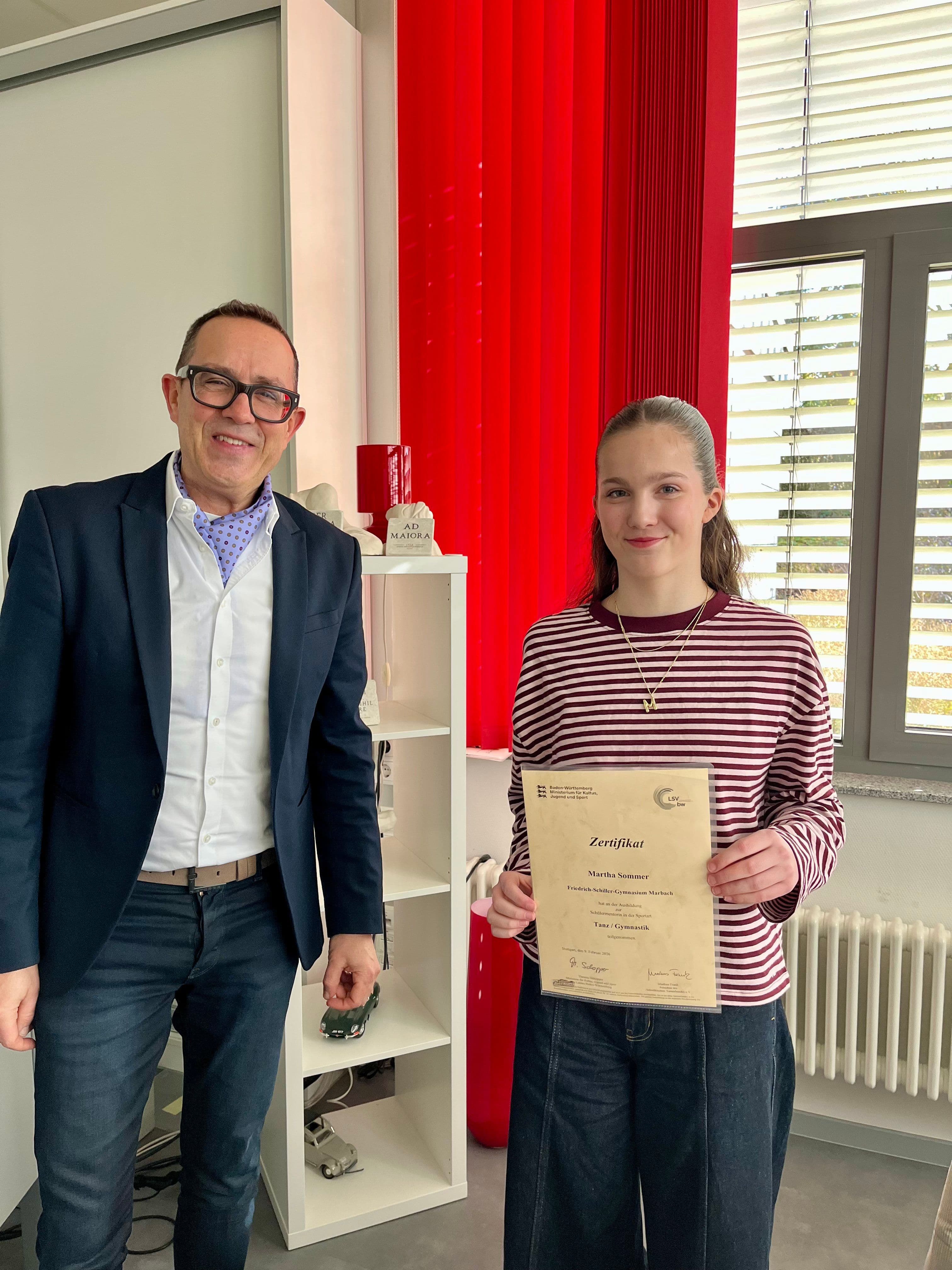 A man in glasses and a young woman in a striped shirt smile, with the woman holding a certificate.