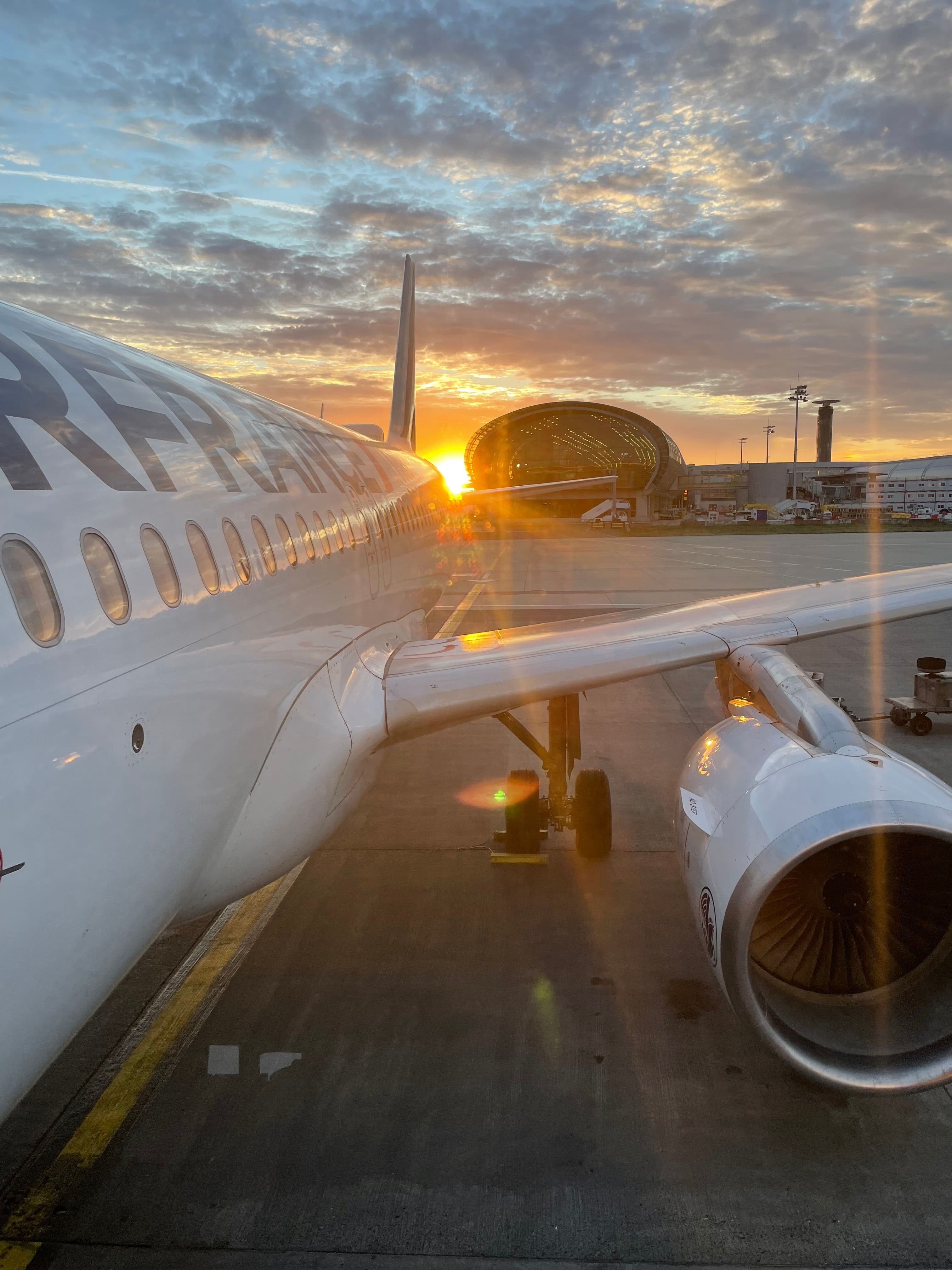 Air France plane on airport tarmac with a bright sunrise behind a dome-shaped terminal.