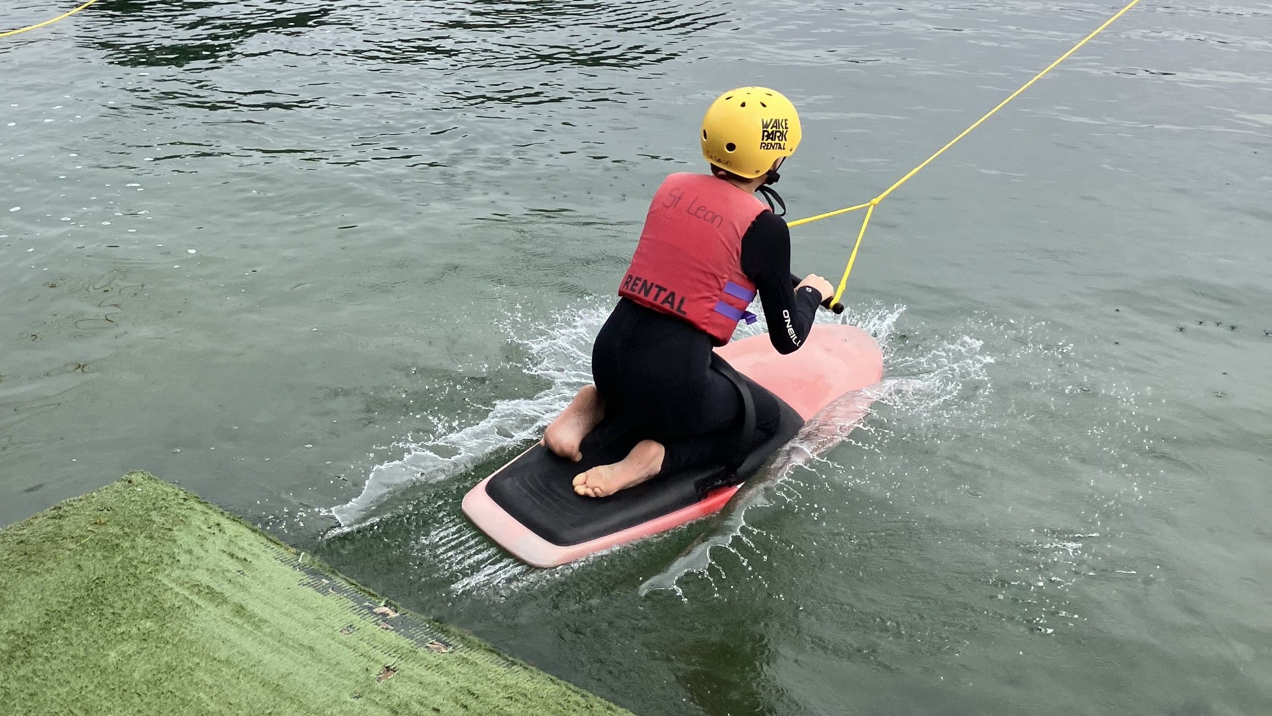 Eine Person startet auf einen Knieboard ins Wasser einer Wasserskianlage