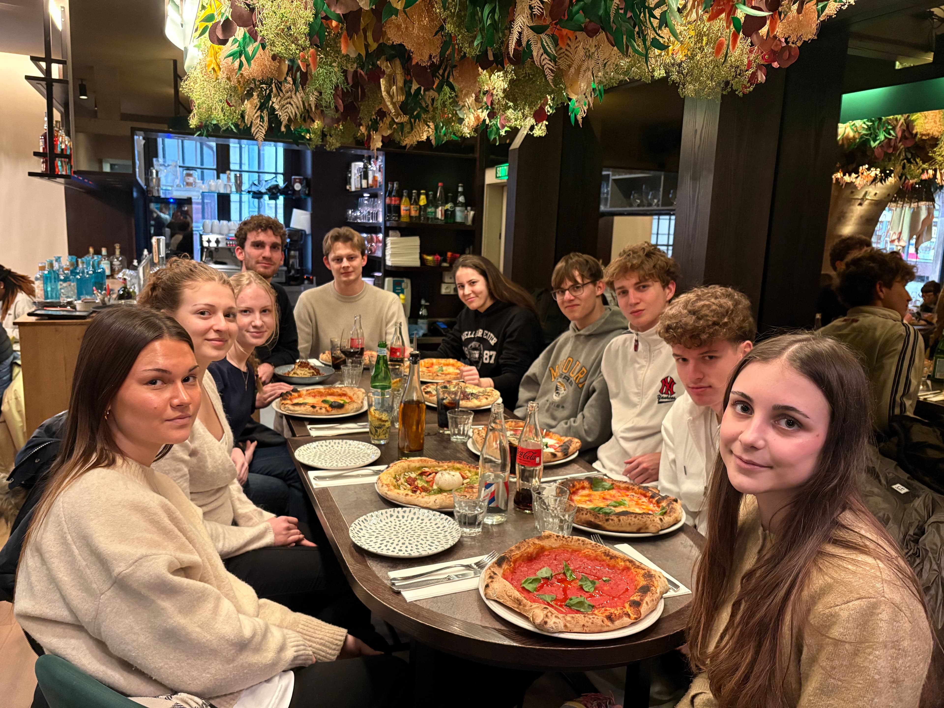 A group of young people enjoying pizzas at an oval table in a restaurant.