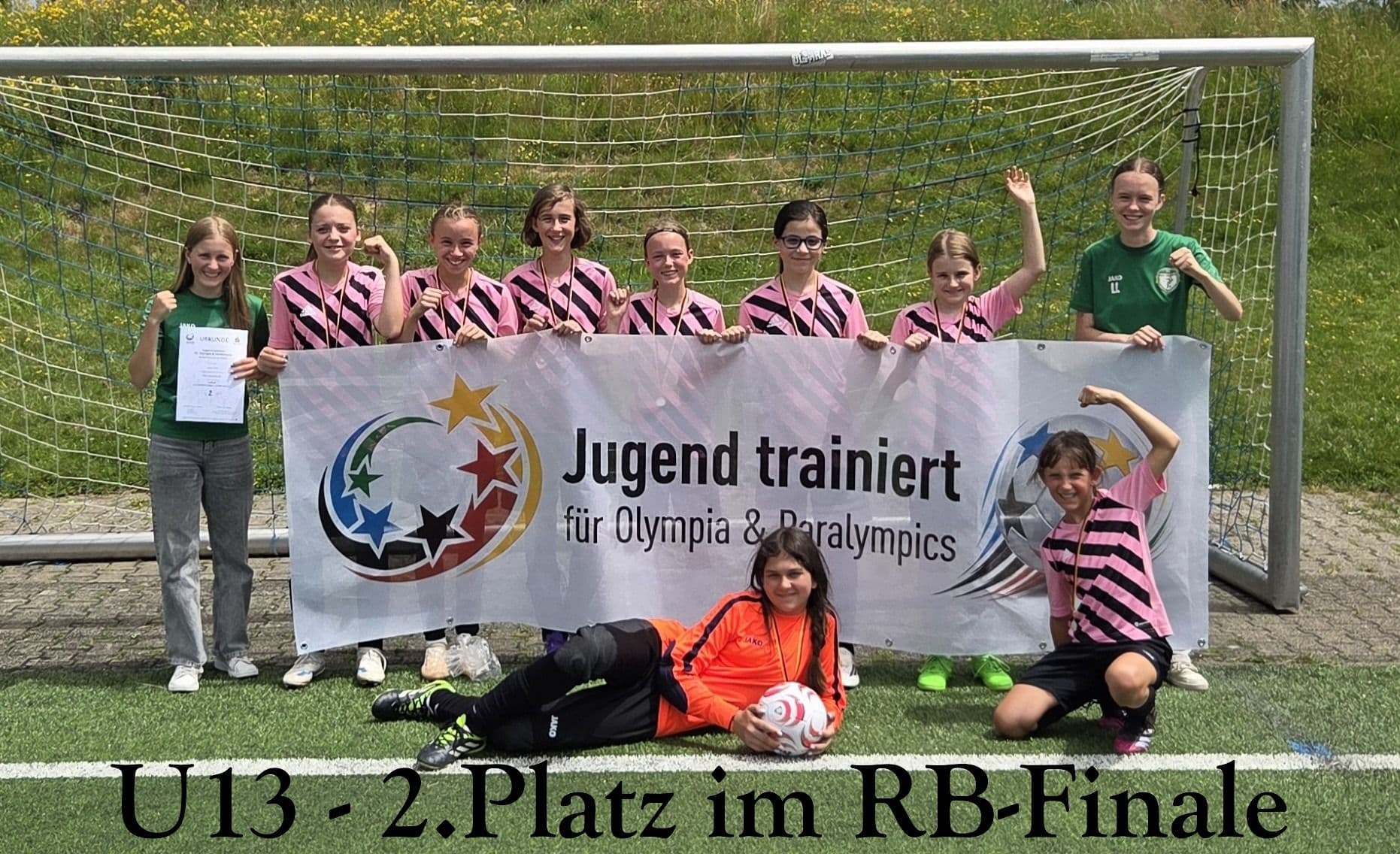 U13 girls soccer team celebrates 2nd place with a "Youth trains for Olympia & Paralympics" banner on a soccer field.