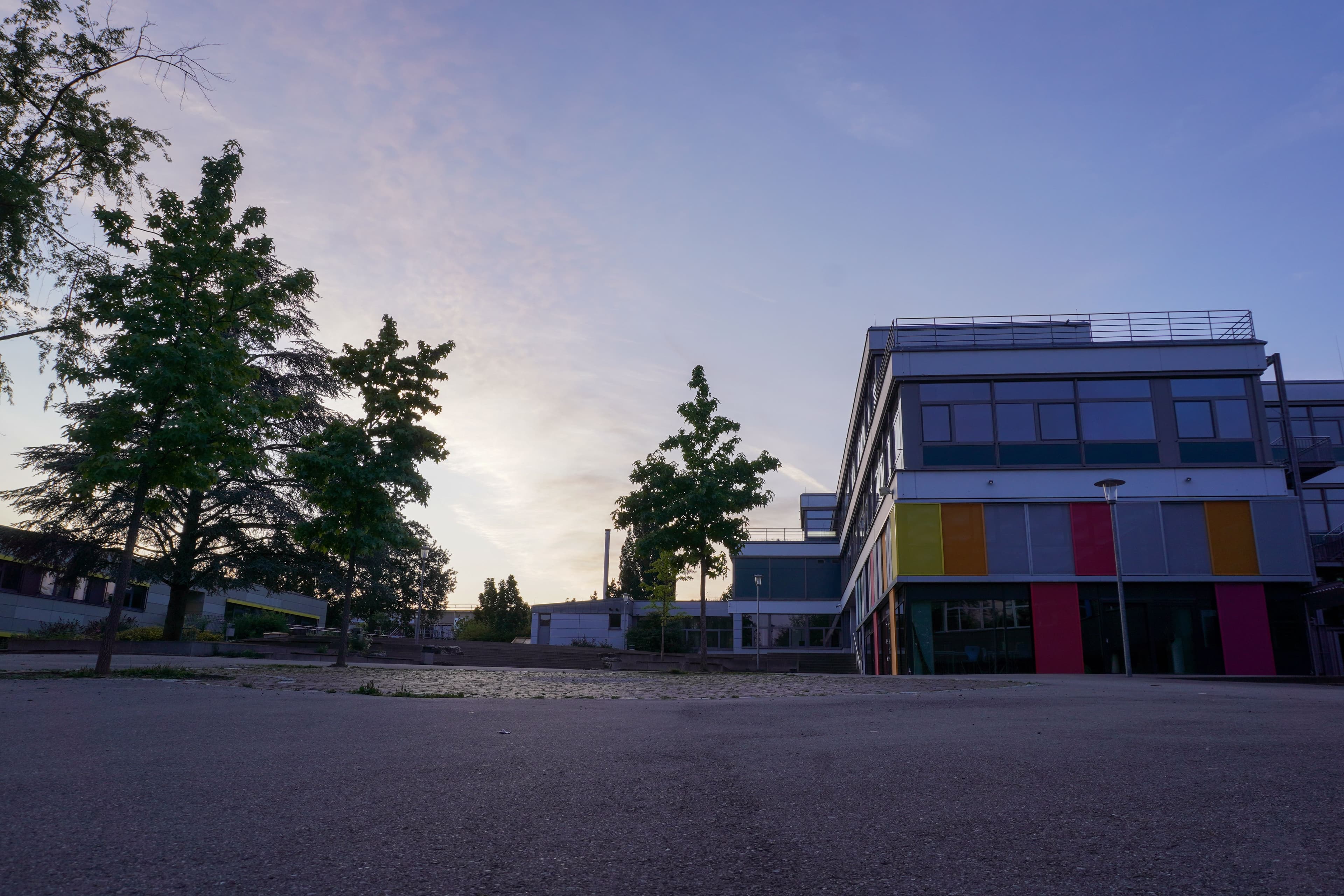 Modern building with colorful panels and trees under a twilight sky.