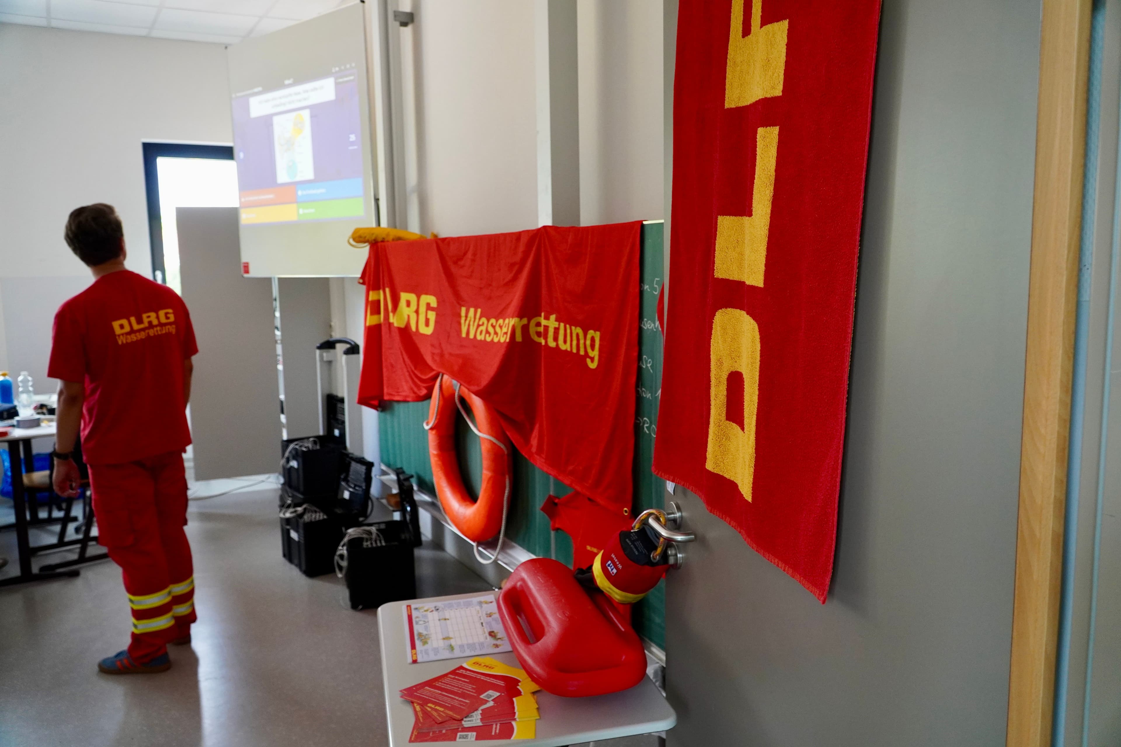 A DLRG water rescue training room with a uniformed person, banners, a lifebuoy, and a rescue tube.