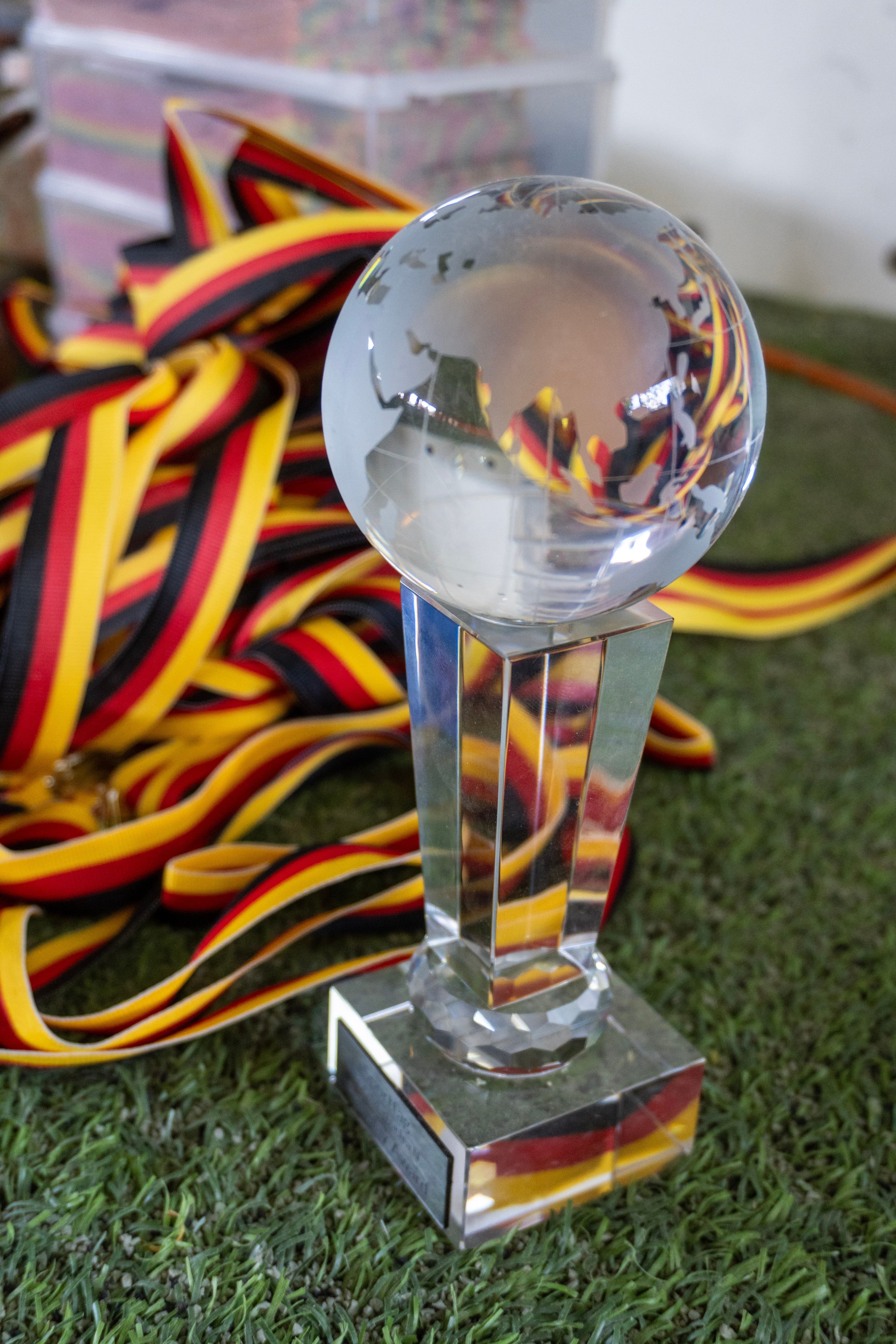 A crystal globe trophy sits on artificial grass, surrounded by numerous red, yellow, and black ribbons.