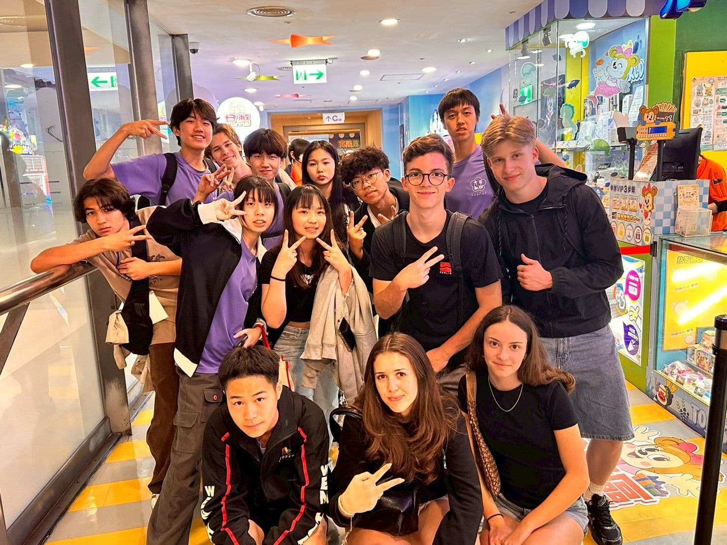A diverse group of young people posing with peace signs in a brightly lit indoor space.