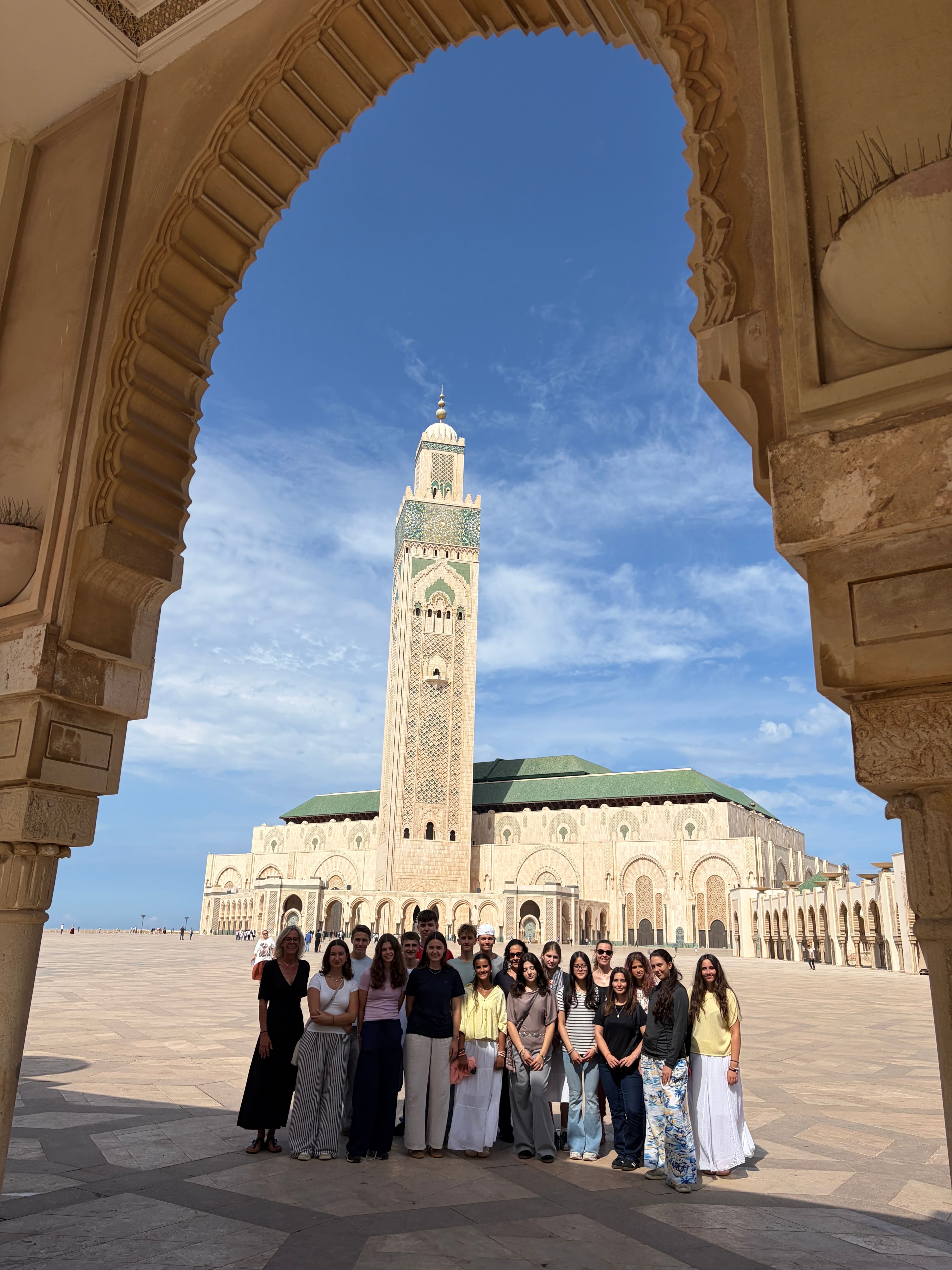A group of people poses in front of the Hassan II Mosque in Casablanca, framed by a decorative archway.