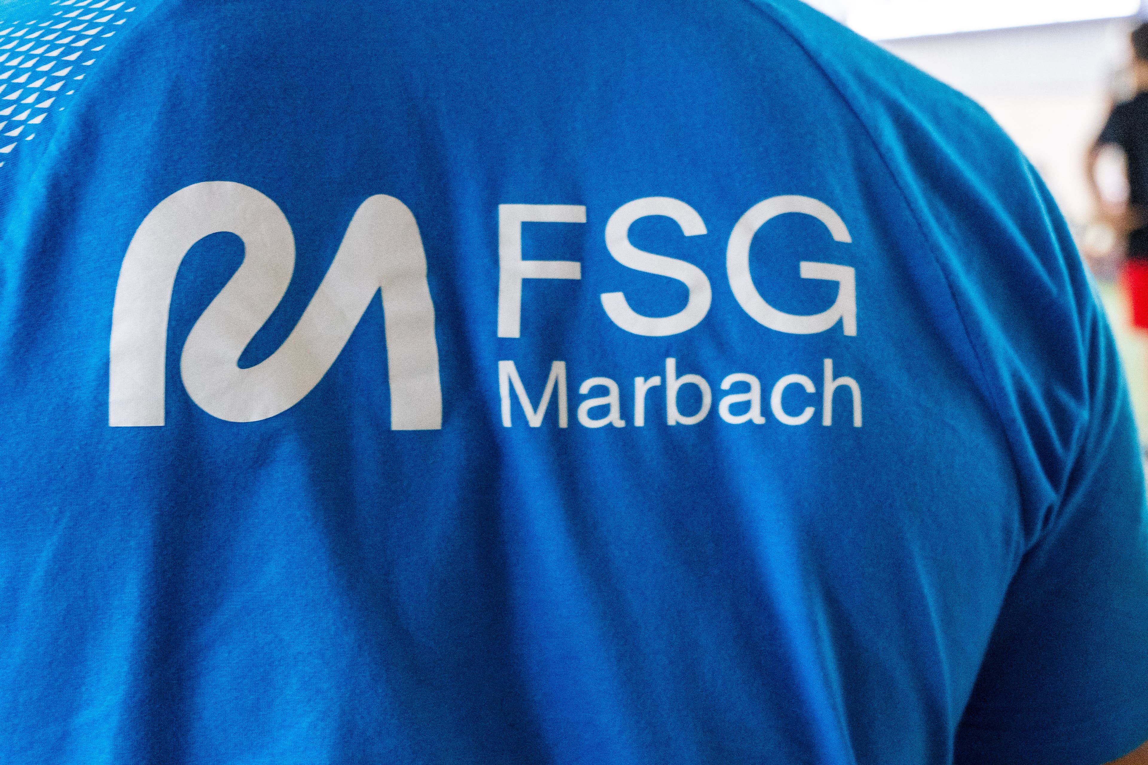 Back of a blue t-shirt with a white stylized M logo and "FSG Marbach" text.